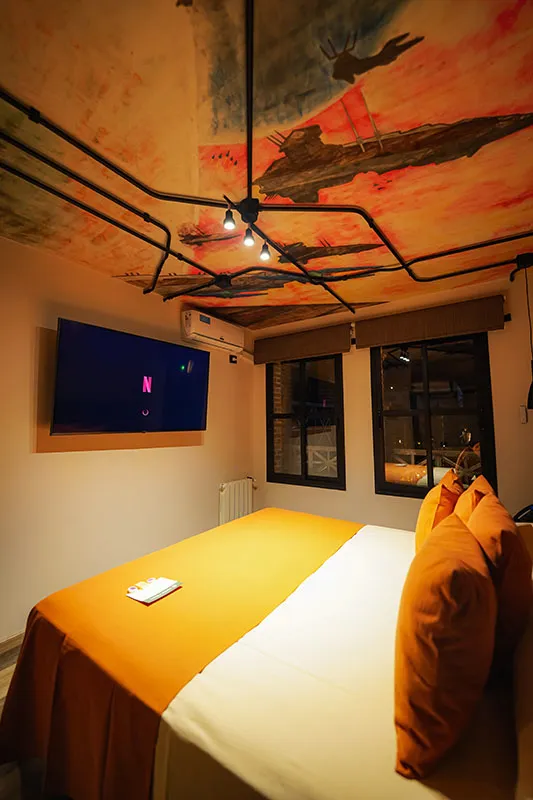Mural celeste y rojo pintado a mano en el techo, sobre la cama y el Smart TV